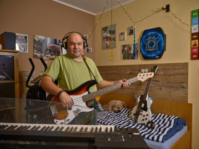 Bewohner in seinem Zimmer spielt E-Gitarre, ein Keyboard steht im Vordergrund